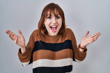 İzole edilmiş arka planda çizgili süveter giyen genç ve güzel bir kadın çılgın ve başarıyı kollarını kaldırıp heyecanla haykırarak kutluyor. Kazanan konsept 