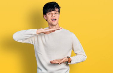 Yakışıklı hippi genç adam sıradan bir kazak giyiyor. Elleri büyük ve büyük bir işaret gösteriyor. Ölçü sembolü. Kameraya bakıp gülümsüyor. ölçüm kavramı. 