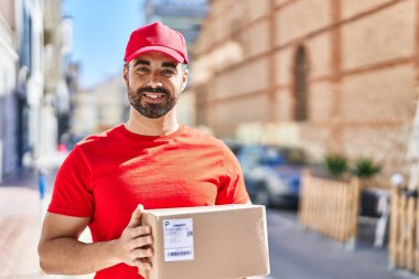 Genç İspanyol kurye sokakta paket tutuyor.