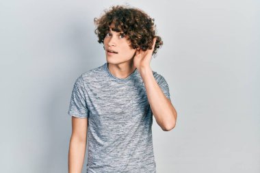 Gri bir tişört giyen yakışıklı genç adam, kulağı kulağında gülümsüyor ve dedikodu ya da dedikoduları dinliyor. Sağırlık kavramı. 