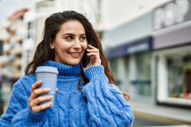 Genç İspanyol kadın akıllı telefondan konuşuyor ve şehirde kahve içiyor..
