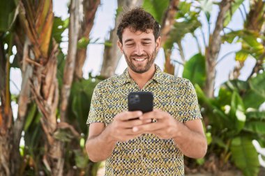 Parkta akıllı telefon kullanarak gülümseyen İspanyol genç adam.