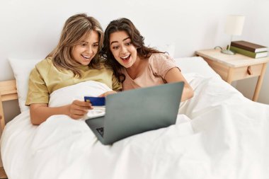 Yatak odasında kredi kartı ve laptop kullanan genç bir çift.