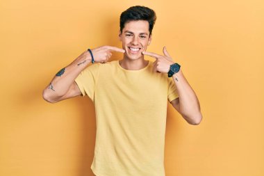Young hispanic man wearing casual yellow t shirt smiling cheerful showing and pointing with fingers teeth and mouth. dental health concept. 