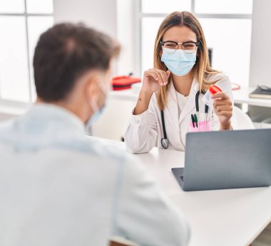 Tıbbi maske takan genç bir adam ve kadın doktor ve hasta klinikte idrar tüpü tutuyorlar.