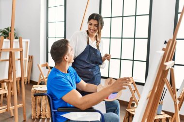 Öğretmen ve engelli boyacı. Tekerlekli sandalyede oturmuş resim yaparken gülümsüyor..