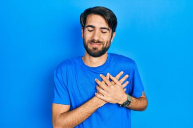 Gündelik kıyafetler giyen genç İspanyol adam elleri göğsünde, gözleri kapalı ve yüzünde minnet dolu bir jest ile gülümsüyor. sağlık kavramı. 