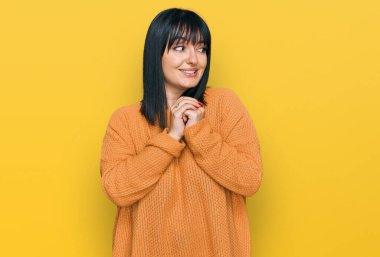 Gündelik kıyafetler giyen genç İspanyol kadın. Gergin ve heyecanlı, elleri çenesinde yan tarafa bakıyor. 