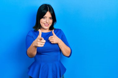 Gündelik kıyafetler giyen genç İspanyol kadın mutlu ve komik yüzüyle kamerayı işaret ediyor. iyi enerji ve titreşimler. 