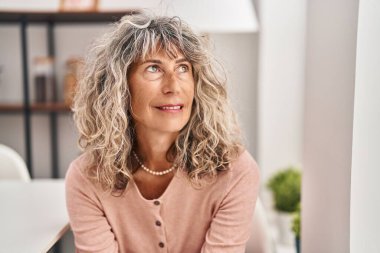 Orta yaşlı bir kadın evdeki sandalyede otururken kendinden emin gülümsüyor.