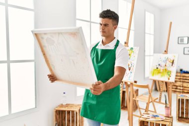 Young hispanic man looking draw canvas at art studio