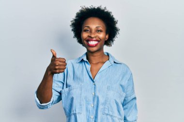 Genç Afrikalı Amerikalı kadın günlük kıyafetler giyiyor mutlu ve pozitif gülümsüyor, başparmağıyla mükemmel ve onay işareti yapıyor. 