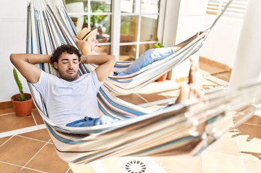 Mutlu gülümseyen genç çift, elleri başlarının üzerinde terasta uzanmış bir şekilde rahatlar..