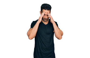 Sakallı İspanyol bir adam, stresten dolayı elleri başının üstünde siyah bir tişört giyiyor. migren ağrısı. 