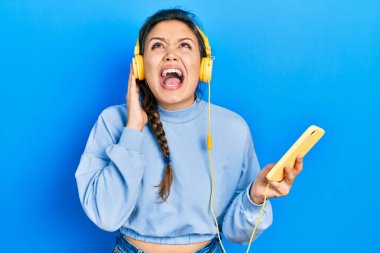 Genç İspanyol kız akıllı telefon ve kulaklık kullanıyor kızgın ve kızgın çığlıklar sinirli ve öfkeli, öfkeyle bağırıyor.. 