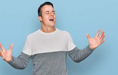 Yakışıklı, kışlık süveter giyen çılgın, deli gibi bağıran, agresif ifadeli ve kollarını kaldırmış genç bir adam. hüsran kavramı. 