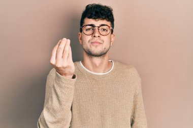 Gündelik kıyafetler ve gözlük takan genç İspanyol adam İtalyan jesti yapıyor. Elleri ve parmakları kendinden emin. 