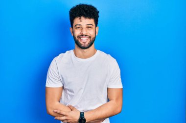 Sakallı, sıradan beyaz tişörtlü genç bir Arap adam gülümsüyor ve kahkahalarla gülüyor.. 