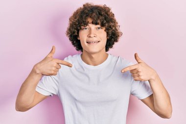 Yakışıklı, beyaz tişört giyen, kendine güvenen, gülümseyen, kendini gururlu ve mutlu gösteren bir genç.. 