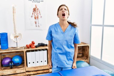 Orta yaşlı İspanyol fizyoterapist kadın ağrı kesici kliniğinde çalışıyor kızgın ve öfkeli çığlıklar atıyor, öfkeyle bağırıyor. öfke ve agresif konsept. 