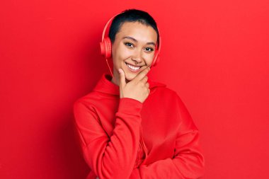 Kısa saçlı, müzik dinleyen, kulaklık takan ve kameraya kollarını kavuşturup gülümseyen güzel İspanyol bir kadın. Olumlu düşünmek. 