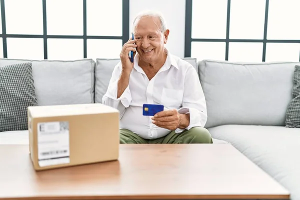 Senior man talking on the smartphone and credit card sitting on sofa at home