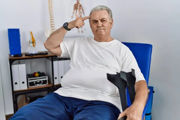 Hombre Caucásico Mayor Clínica Fisioterapia Sosteniendo Muletas Sonriendo Apuntando Cabeza —  Fotos de Stock