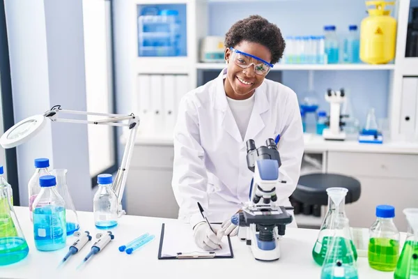African American Woman Wearing Scientist Uniform Using Microscope Write Clipboard — Fotografia de Stock