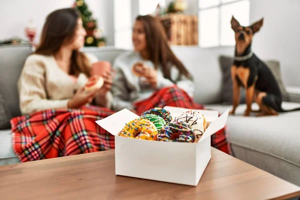 Two women having breakfast sitting with dog by christmas tree at home