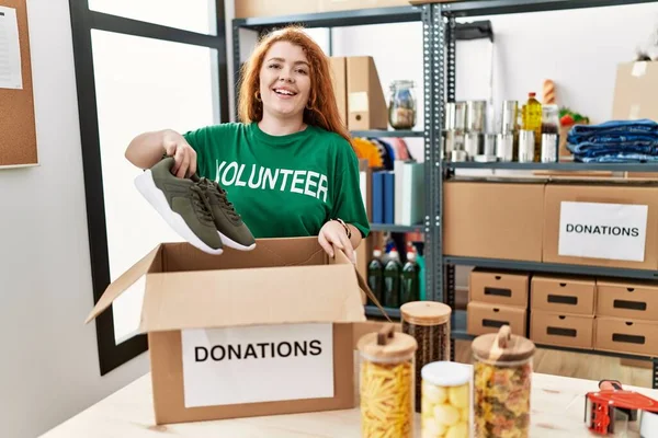 Young Redhead Woman Wearing Volunteer Shirt Holding Second Hand Sneakers — Stock Photo, Image