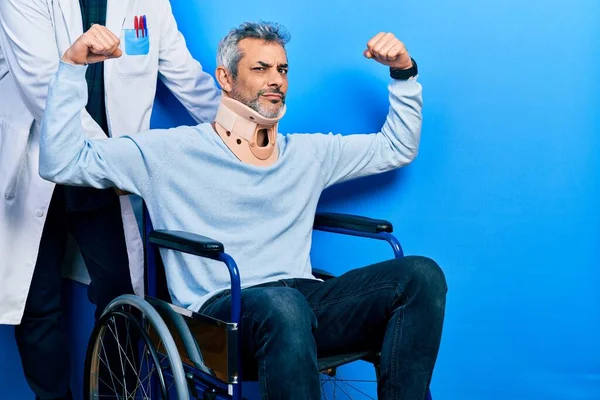 Handsome middle age man with grey hair on wheelchair wearing cervical collar showing arms muscles smiling proud. fitness concept.