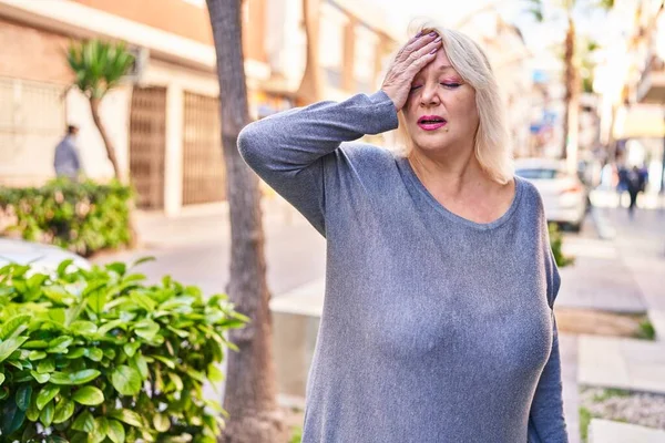 Middle age blonde woman with headache at street