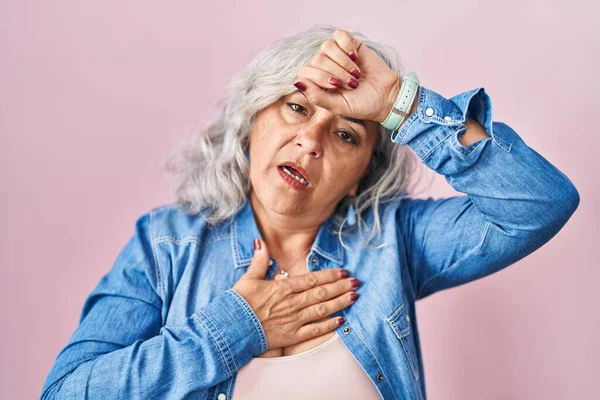 白髪の中年女性はピンクの背景の上に立っている病気や発熱 インフルエンザや風邪 ウイルス病のために額に触れる — ストック写真