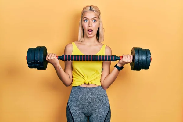 Beautiful Blonde Woman Wearing Sportswear Using Dumbbells Afraid Shocked Surprise — Foto Stock