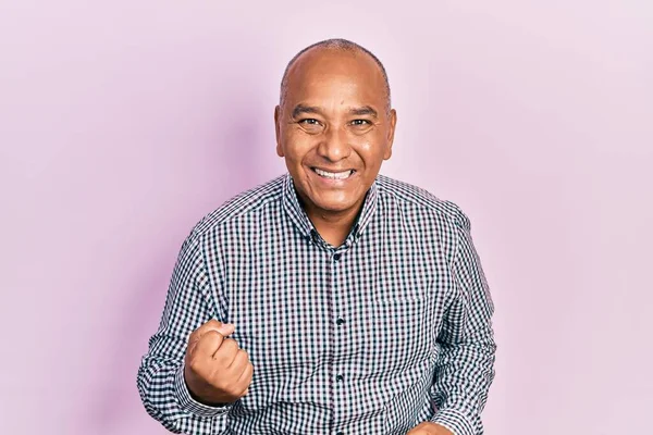 Orta yaşlı, gündelik kıyafetler giyen, mutlu ve heyecanlı bir Latin adam kolları havada, gülümseyen ve başarı için bağıran, kazanan bir jest yapıyor. kutlama konsepti. 