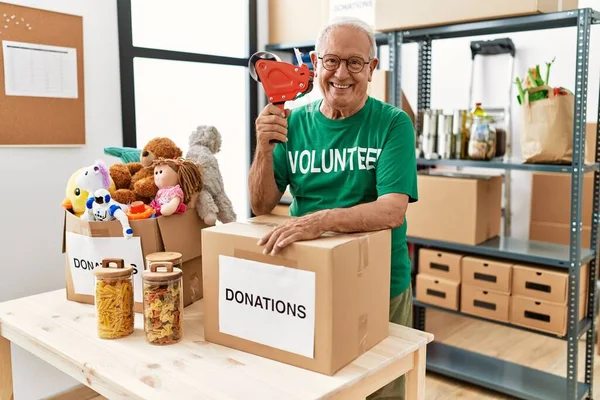 Senior Man Draagt Vrijwillige Uniform Verpakking Donaties Kartonnen Doos Bij — Stockfoto
