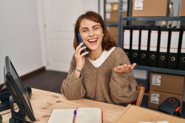 Kafkasyalı genç kadın ecommerce işçisi ofisteki akıllı telefondan konuşuyor.