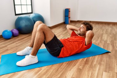 Genç İspanyol adam gülümsüyor spor merkezinde kendine güvenen karın kasları egzersizi yapıyor.