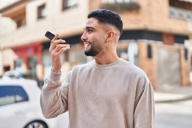 Genç Arap adam gülümsüyor, kendinden emin bir şekilde caddedeki akıllı telefondan konuşuyor.