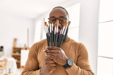Genç Afrikalı Amerikalı sanatçı, resim stüdyosunda yüzünü boya fırçasıyla kaplıyor..