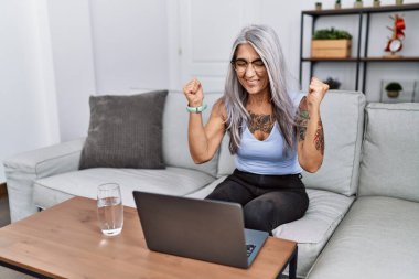 Orta yaşlı, kır saçlı bir kadın evde dizüstü bilgisayar kullanarak başarıyı kutluyor. Kollarını kaldırmış, gözlerini kapatmış heyecanlı çığlıklar atıyordu. Kazanan konsept 