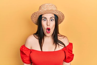 Young hispanic woman wearing summer hat afraid and shocked with surprise expression, fear and excited face. 