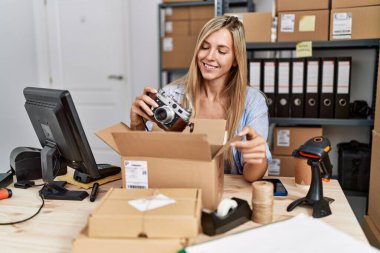 Young blonde woman ecommerce business worker packing vintage camera on order package at office