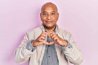 Orta yaşlı, sıradan kıyafetler giyen, aşık gülümseyen, elleriyle kalp sembolü yapan Latin bir adam. romantik kavram. 