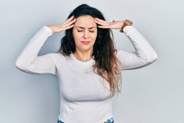 Elleri başının üstünde, günlük kıyafetler giyen genç İspanyol kadın, stres yüzünden baş ağrısı çekiyor. migren ağrısı. 
