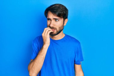 Günlük kıyafetler giyen genç İspanyol adam gergin ve gergin görünüyor. Ağzı tırnak yiyen eller. anksiyete. 