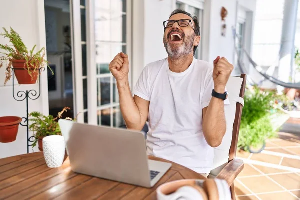 Middle age man using computer laptop at home celebrating surprised and amazed for success with arms raised and eyes closed. winner concept.