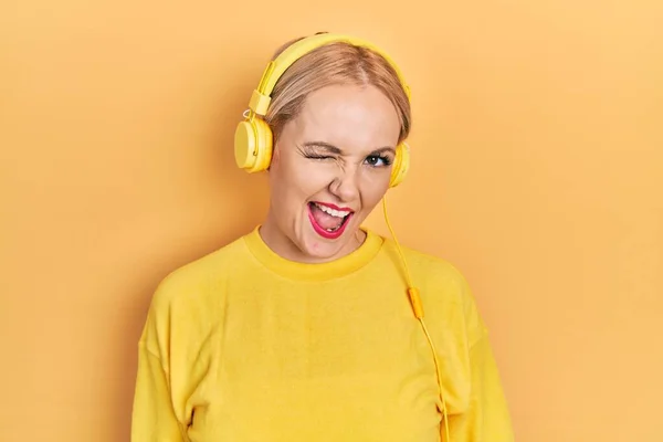 Mujer Rubia Joven Escuchando Música Usando Auriculares Guiñando Ojo Mirando —  Fotos de Stock