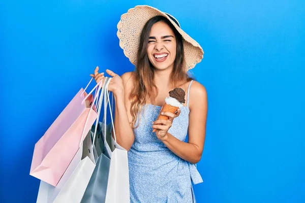 Young hispanic girl holding shopping bags and ice cream smiling and laughing hard out loud because funny crazy joke.