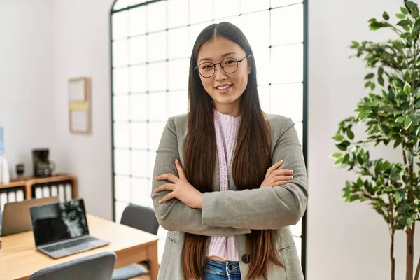 Young chinese businesswoman smiling happy standing with arms crossed gesture at the office.